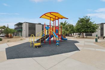 Shaded playground featuring slides, climbing elements, and soft-surface play area